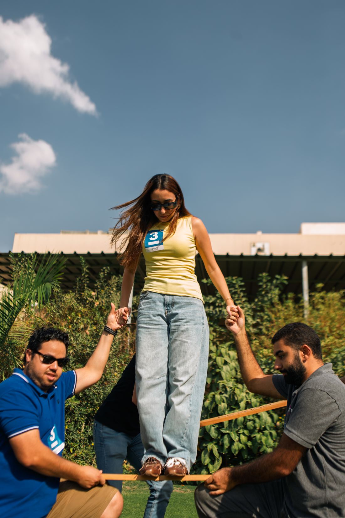 A participant balancing on a beam, held steady by teammates