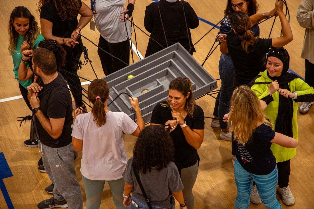 Team guiding a ball through an overhead rope-and-maze puzzle